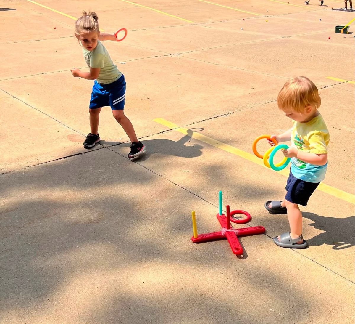 Two children playing ring toss on a sunny outdoor play pad.